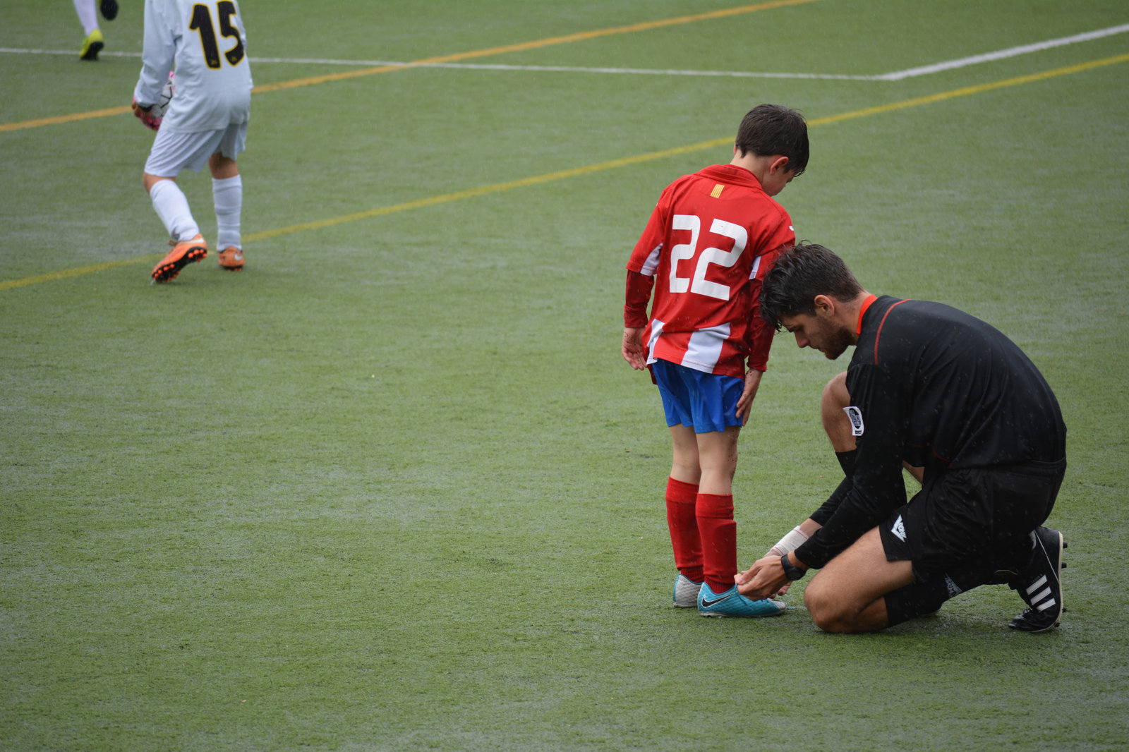 Man tying boy's shoe laces in a football field