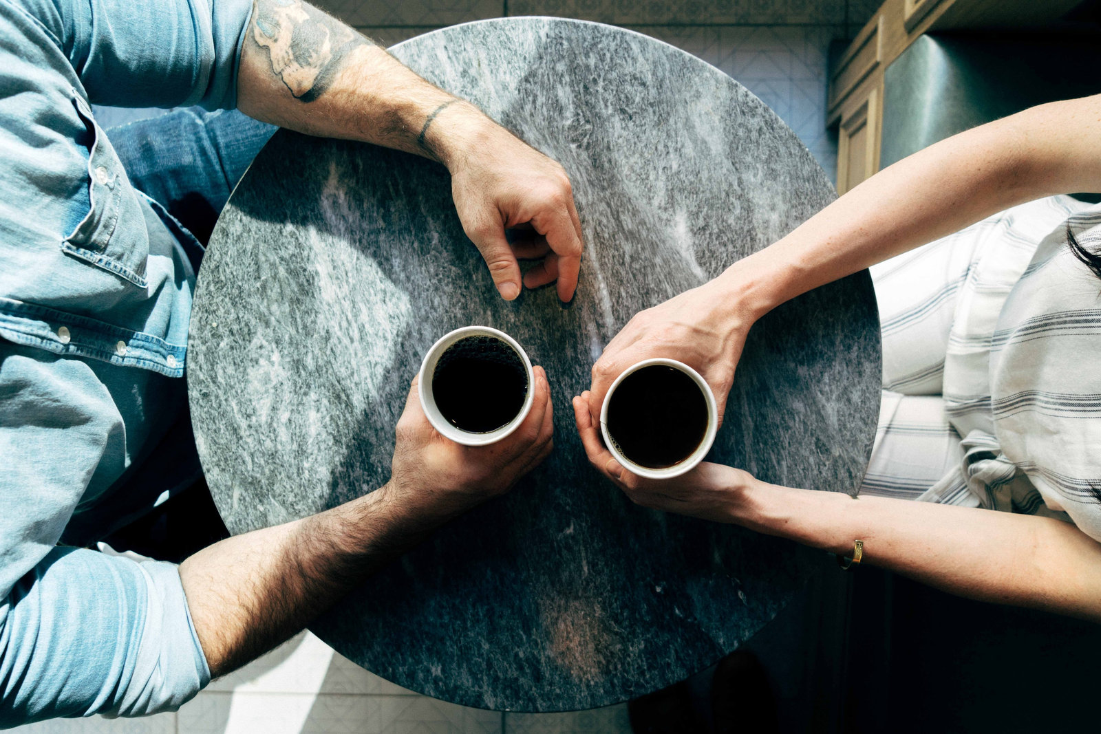 Two people holding coffees, shot from above the table